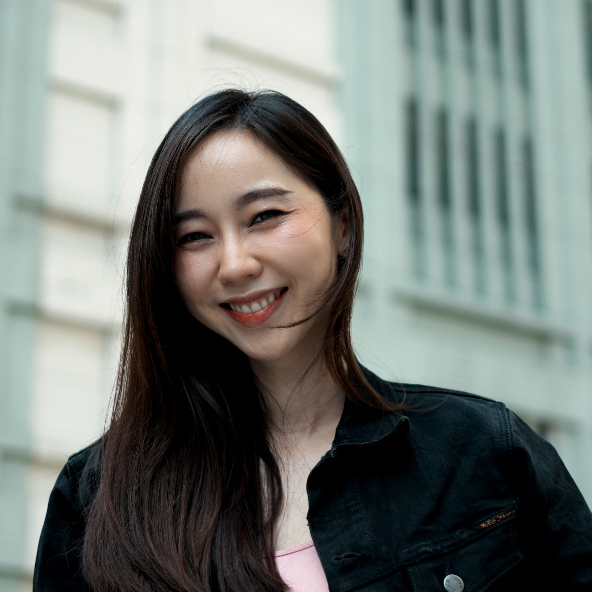 Close-up of girl with long hair, in a black jacket and pink top, smiling at the camera 