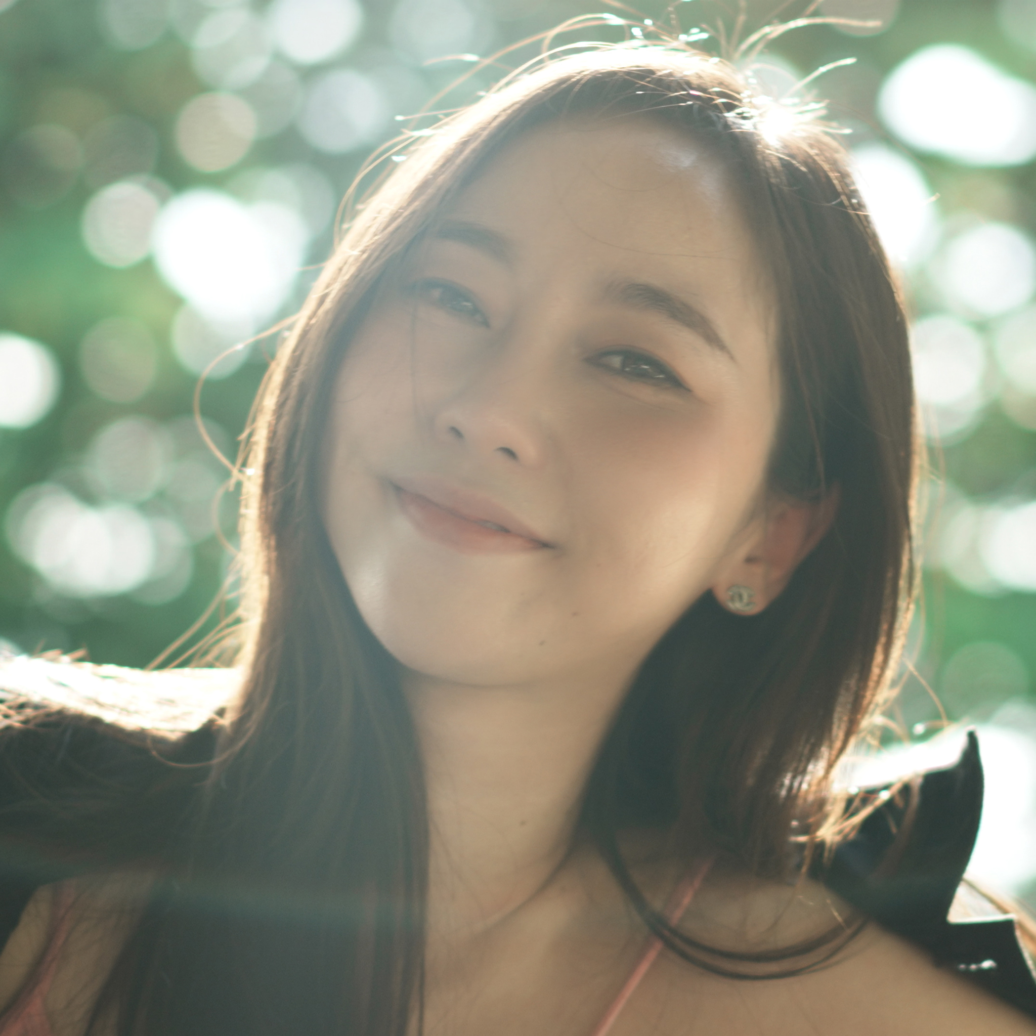 Close-up of girl with long hair, sitting down and leaning slightly backwards in a bright, outdoor environment