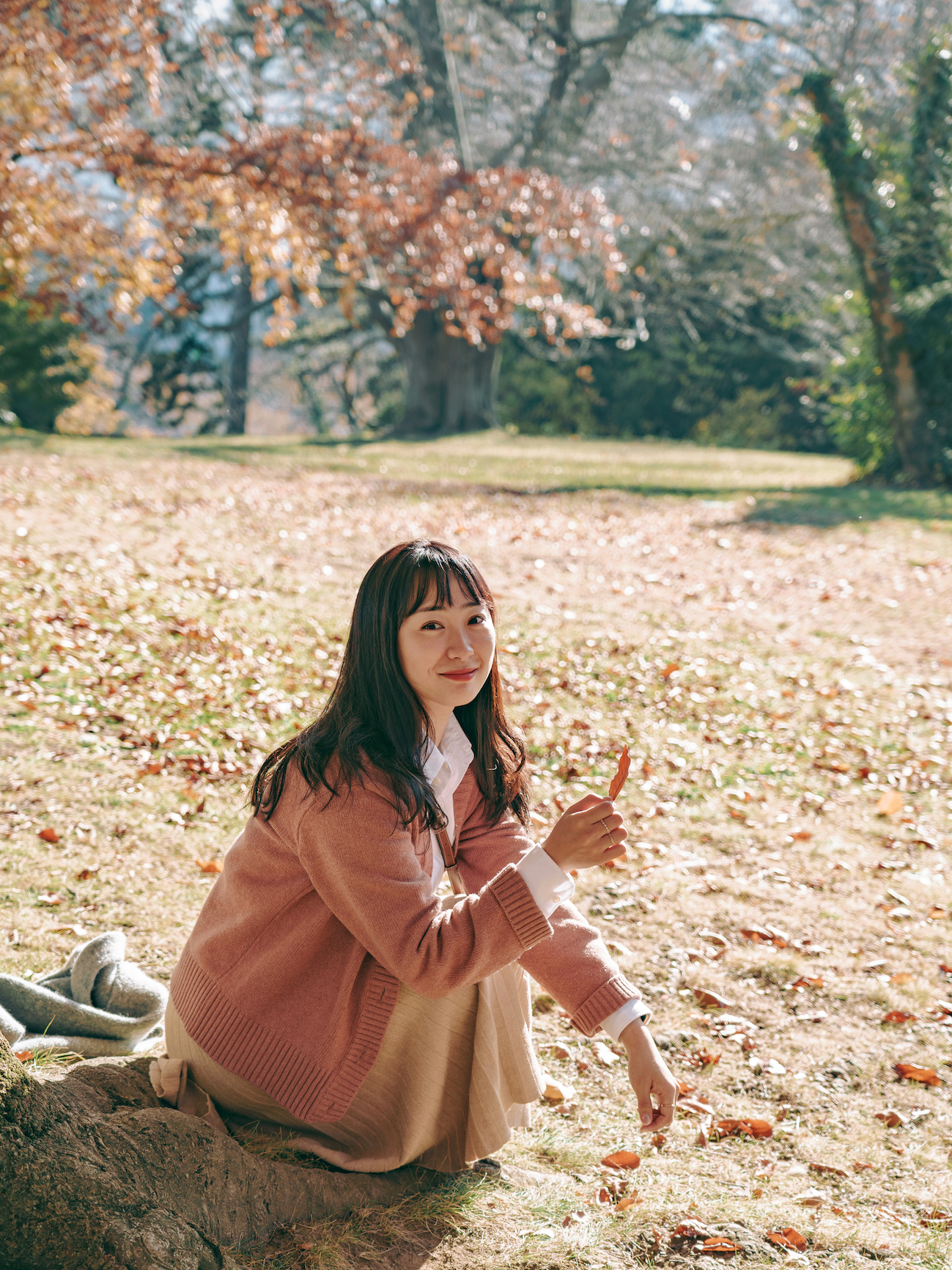 Girl crouched on the floor, holding up a fallen leaf and looking at the camera