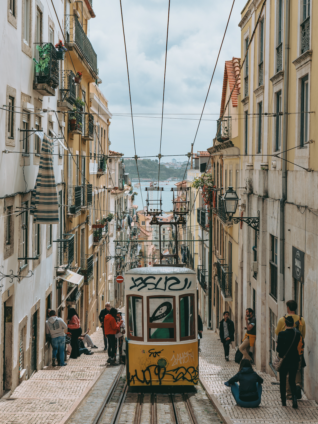 Tram moving downhill on a slope between buildings with pedestrians on the side