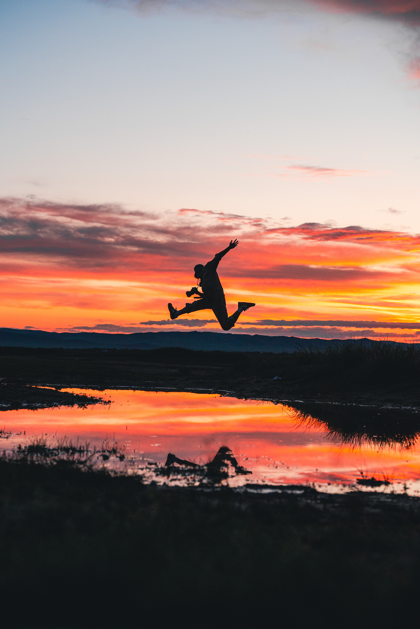 Silhouette of a man jumping in front of a lake at sunset