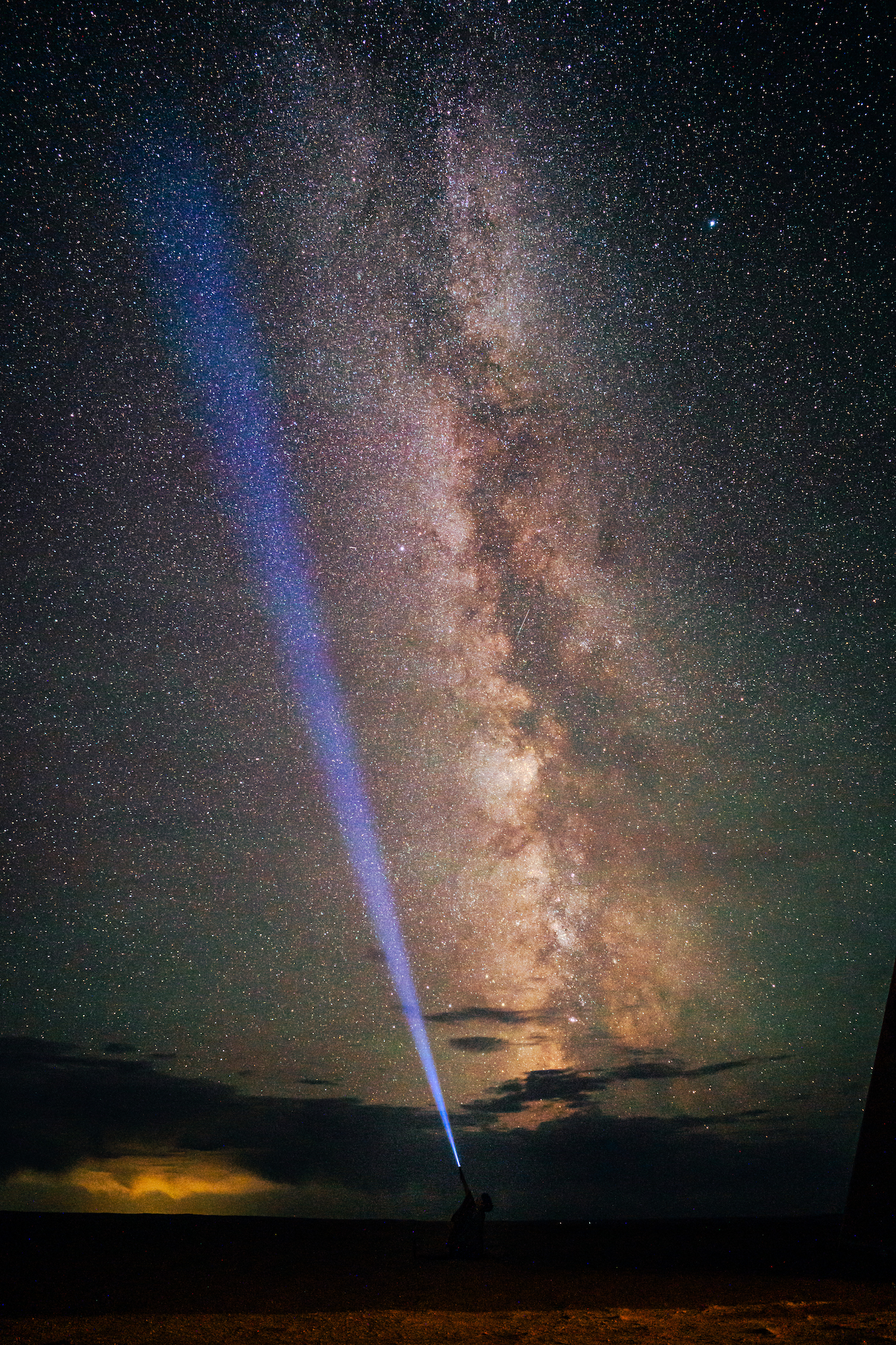 Light shining from a torchlight up at the vast, starry night sky