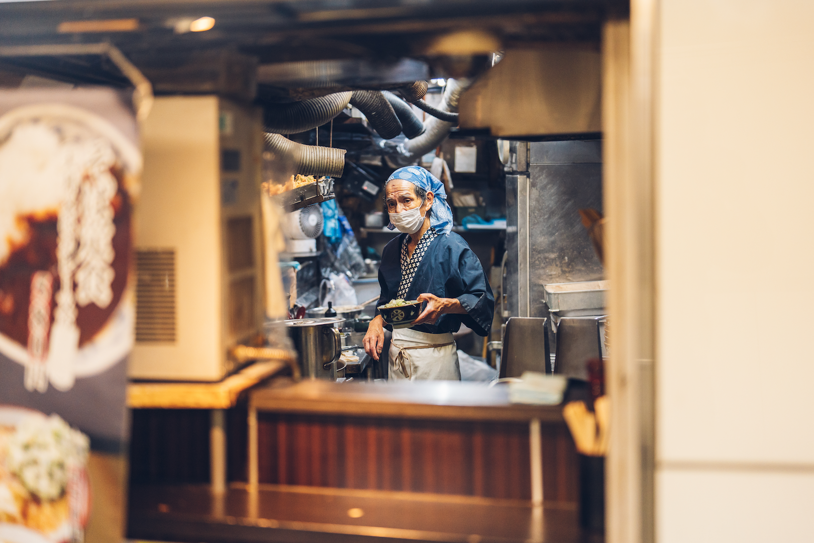 Ramen master preparing a bowl of ramen noodles in a narrow, full kitchen