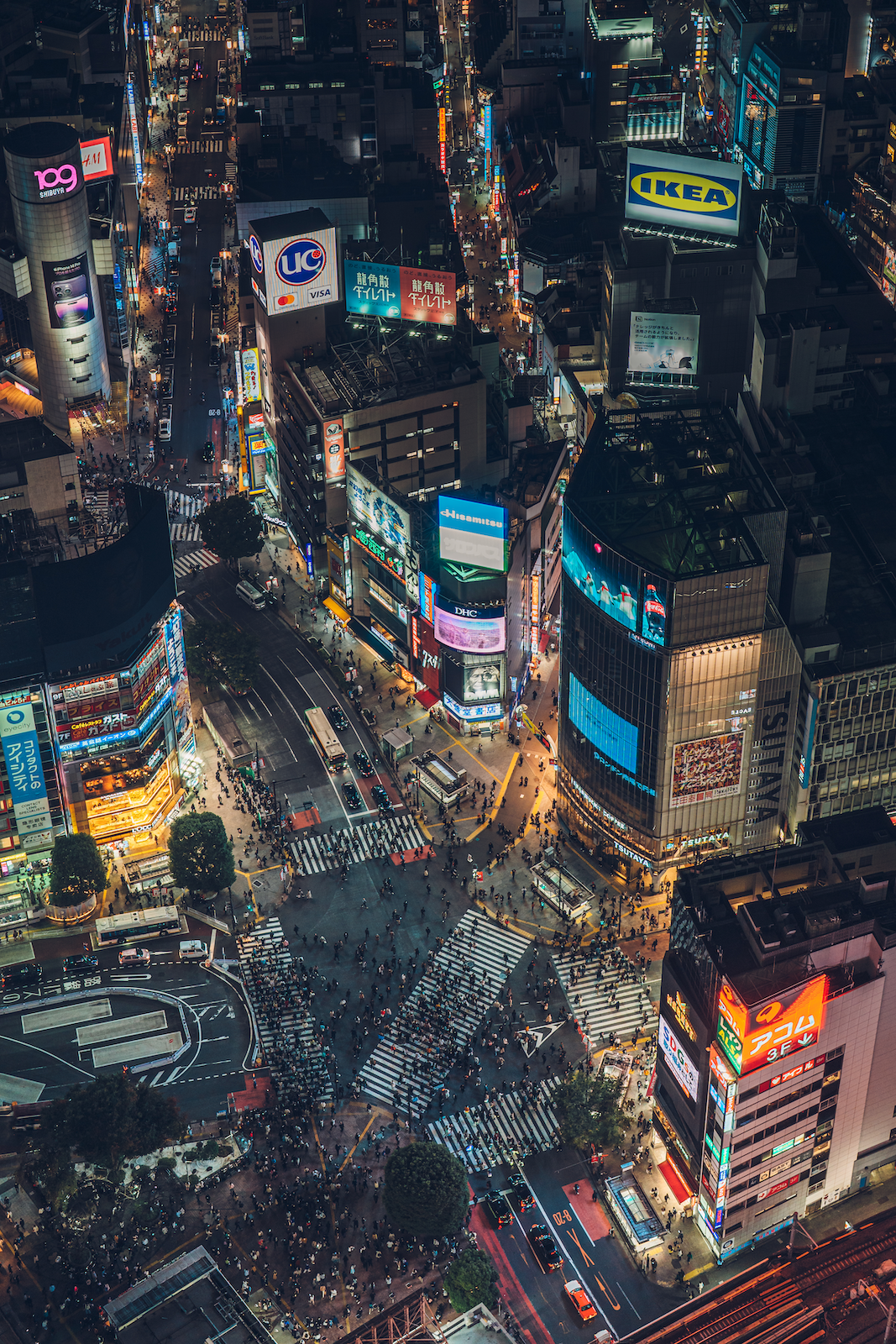 Aerial view of Shibuya at night, with a large crowd moving across the Shibuya Scramble Crossing